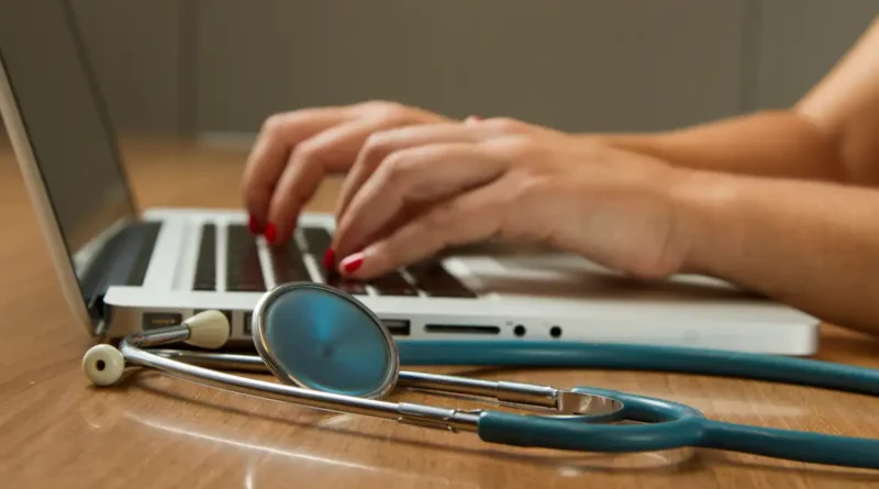 Médica digita no computador, tendo seu estetoscópio ao lado. Foto: National Cancer Institute/Unsplash