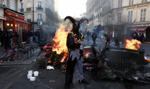 A demonstrator wearing a costume stands in front of burning flames, in Paris, France, October 18, 2026. REUTERS/Abdul Saboor