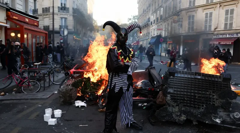 A demonstrator wearing a costume stands in front of burning flames, in Paris, France, October 18, 2026. REUTERS/Abdul Saboor