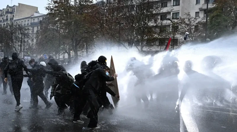 Protesters take cover behind a plywood board as French riot police use a water canon amid clashes during an authorised demonstration organised by labour unions in Paris as part of nationwide protests called by the